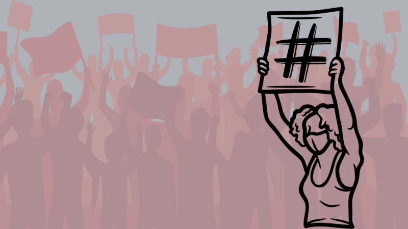 The image you shared shows a group of people in the background holding up signs and banners, with one person in the foreground prominently holding up a sign with a large hashtag symbol (#) on it. The person in the foreground is wearing a mask.