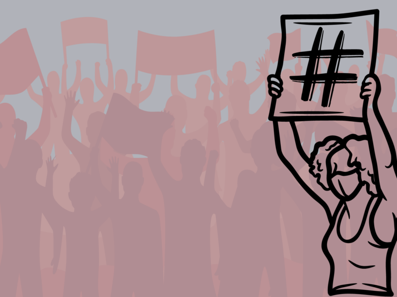 The image you shared shows a group of people in the background holding up signs and banners, with one person in the foreground prominently holding up a sign with a large hashtag symbol (#) on it. The person in the foreground is wearing a mask.