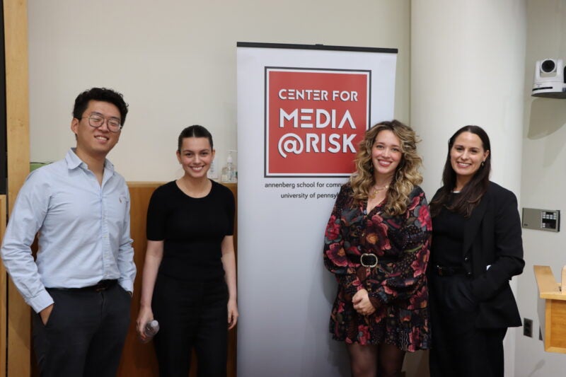 four people standing and smiling around the media at risk banner