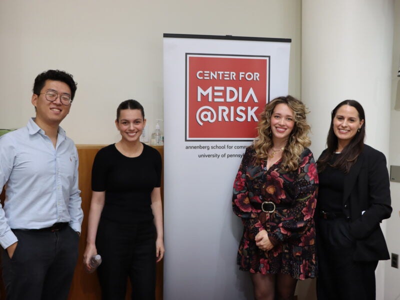 four people standing and smiling around the media at risk banner